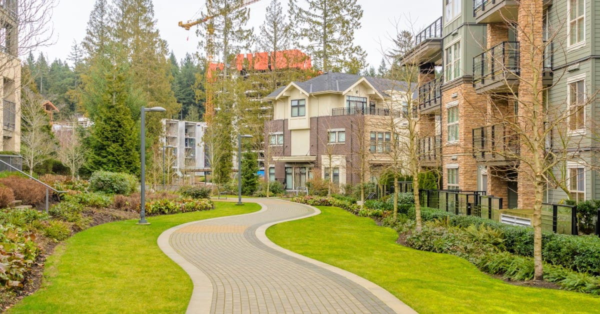 A modern three-story apartment complex features a well-maintained landscape with a brick walkway and nearby construction.